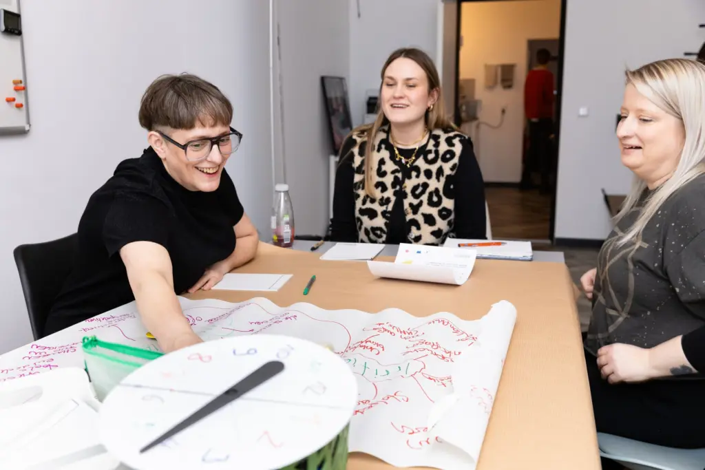 Drei Frauen an einem Tisch, sie lachen und basteln mit den auf dem Tisch liegenden Materialien.