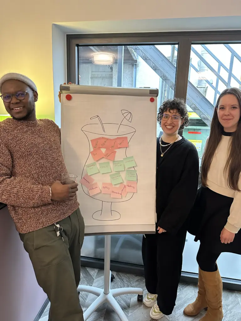 Zwei Frauen und ein Mann vor einer FLipchart, sie lächeln.