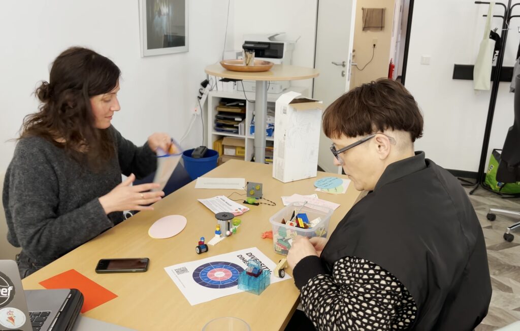 Zwei Personen sitzen an einem Tisch und bauen mit Lego an einem Modell.